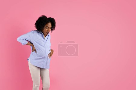 Photo for Sad desperate young black pregnant woman in casual touching big belly with hand, suffering from pain and contractions, isolated on pink studio background. Childbirth, expect baby, problems - Royalty Free Image