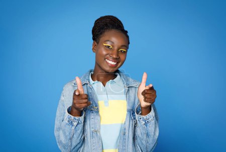 Foto de Positivo fresco atractivo joven afroamericana mujer en traje casual elegante apuntando a la cámara y sonriendo aislado sobre fondo azul, espacio de copia. Gen Z concepto de estilo de vida - Imagen libre de derechos