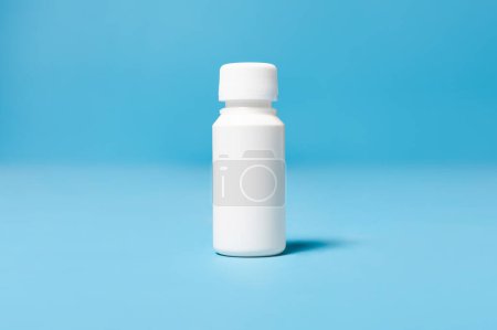 Foto de Frasco blanco cerrado de plástico blanco medicinal 100 ml aislado sobre fondo estudio azul, espacio de maqueta para su diseño, texto y publicidad - Imagen libre de derechos