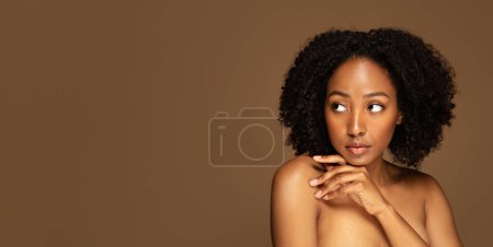 Photo for Sexy attractive young african american woman posing topless on brown studio background, touching her shoulder, enjoying silky smooth body skin after SPA treatment, looking at copy space, banner - Royalty Free Image