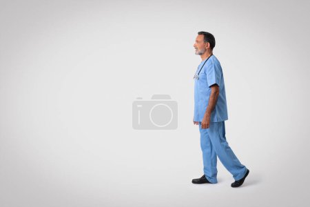 Téléchargez les photos : Sérieux caucasien médecin chirurgien principal en uniforme bleu regardant l'espace vide, isolé sur fond gris, pleine longueur, studio. Médecine, soins de santé, travail professionnel, examen - en image libre de droit