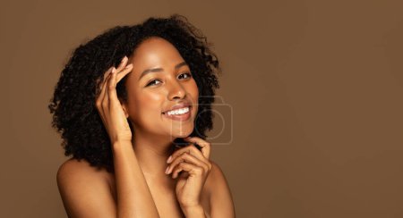 Téléchargez les photos : Concept de médecine esthétique et de chirurgie esthétique. Joyeux attrayant jeune femme noire avec les cheveux bouclés et la peau parfaite posant seins nus sur fond de studio brun, espace de copie, bannière - en image libre de droit