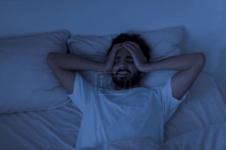 Photo for Sleeping Problem. Stressed young indian man lying alone in bed and touching head, millennial eastern guy awake in the night, feeling depressed, suffering from insomnia or mental problems - Royalty Free Image
