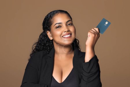 Photo for E-banking, e-commerce. Happy latin chubby businesswoman bank manager holding credit card for online payments, shopping, loan, startup, mortgage, cashback isolated on brown background - Royalty Free Image