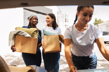 Photo for Three cheerful multiracial women girlfriends moving to new apartment, young ladies flatmates packing paper boxes with their stuff belongings into car trunk, have conversation. Relocation concept - Royalty Free Image