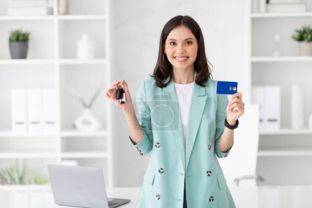 Photo for Glad millennial european businesswoman recommending credit card and keys of car in white office interior. Work, profit finance for business, buying auto, rent transport, ad, offer - Royalty Free Image