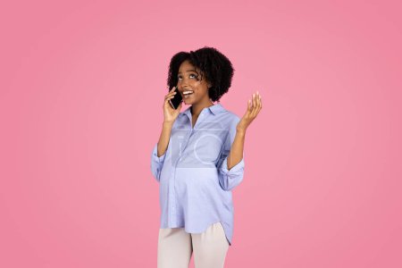 Photo for Cheerful young black pregnant woman in casual with belly, call by smartphone, isolated on pink studio background. Device, expect baby, good news, gossip and communication, ad, offer - Royalty Free Image