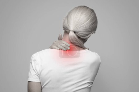 Photo for Rear view of tired mature woman touching inflamed zone on her neck, suffering from cervical osteochondrosis, massaging and rubbing sore area lightened with red, monochrome shot, copy space - Royalty Free Image