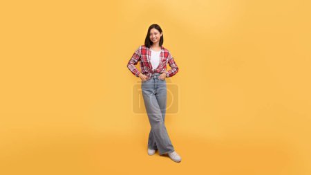 Photo for Full length shot of happy lady in casual outfit posing holding hands in pockets and smiling at camera standing isolated on yellow background, panorama, free space - Royalty Free Image