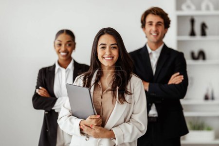 Photo for Leadership. Successful latin businesswoman holding laptop in hands, standing with diverse business team in office. Career growth motivation, entrepreneurship concept - Royalty Free Image