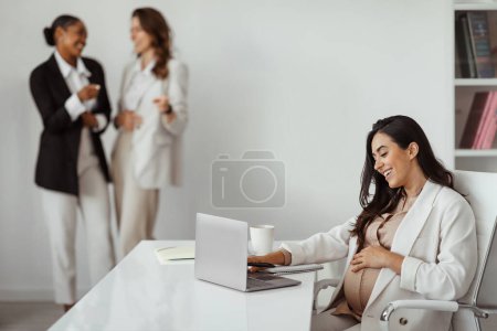 Téléchargez les photos : Femmes d'affaires pointant vers la femme enceinte travaillant sur ordinateur portable au bureau. Collèges intimidation, exclusion des victimes d'employés ou harcèlement et discrimination des travailleurs - en image libre de droit