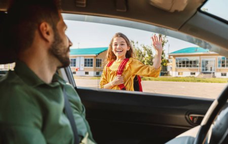 Photo for Parenthood and morning routine. Cheerful girl elementary school learner going to school, waving goodbye to her father sitting in the car, focus on schoolgirl - Royalty Free Image