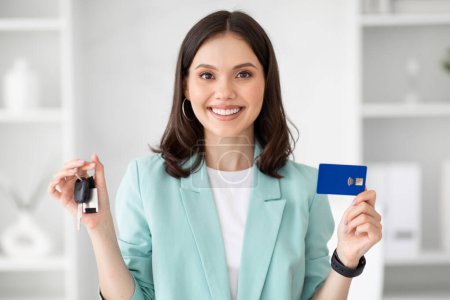 Photo for Positive millennial european businesswoman manager recommending credit card and car keys, in white office interior. Buying new auto, work, loan, profit and finance for business - Royalty Free Image