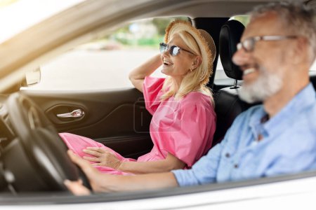 Photo for Smiling positive senior couple husband and wife going summer vacation by car together. Happy retired man and woman wearing wicker hat and sunglasses sitting in auto, enjoying road trip, chatting - Royalty Free Image