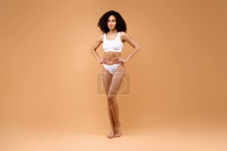 Téléchargez les photos : Slim jeune femme latine en lingerie blanche posant sur fond brun, dame jouissant de sa beauté naturelle et de la féminité, plan complet, espace libre - en image libre de droit