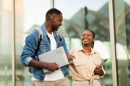 Téléchargez les photos : Heureux amoureux jeunes étudiants couple noir frineds marcher par la rue, ont rendez-vous après les cours à l'université. gai afro-américain homme et femme aller à l'université ensemble, bavarder - en image libre de droit