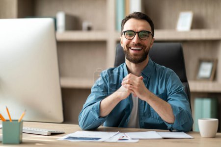 Photo for Modern Businessman. Portrait Of Handsome Young Man Posing At Desk In Office, Happy Millennial Male Entrepreneur Wearing Eyeglasses Sitting At Workplace, Looking At Camera And Smiling - Royalty Free Image