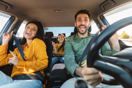 Foto de Nos vamos de vacaciones. Familia feliz de tres personas conduciendo en su automóvil, bailando con música y cantando su canción favorita, disfrutando viajar en coche - Imagen libre de derechos