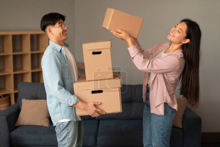 Photo for Positive Young Asian Couple Packing For Moving, Woman Giving Carton Boxes To Husband, Carrying Belongings Standing At Modern Home Interior. Real Estate, Relocation And Apartment Rent Offer Concept - Royalty Free Image