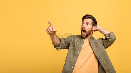Photo for Shocked european middle aged man with open mouth touching head and pointing finger at empty space, isolated on yellow background, panorama. Human emotions, huge sale, great news, offer and ad - Royalty Free Image