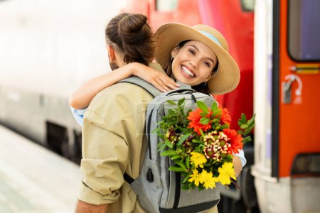 Photo for Happy young european guy meets lady from train, hugs, gives flowers at station. Come back from tour, tourist emotions, lifestyle, summer vacation, love and relationship emotions - Royalty Free Image