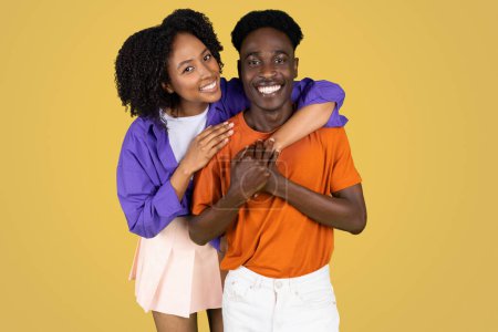 Photo for Cheerful millennial black lady hugging boyfriend in casual, enjoy success, date, isolated on yellow studio background. Human emotions, lifestyle, ad and offer, love and relationships - Royalty Free Image