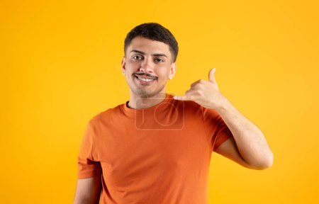 Téléchargez les photos : Homme brésilien joyeux gesticulant Call Me, tenant la main comme un téléphone près de l'oreille et souriant, posant sur fond jaune. Contact, numéro de téléphone et concept de communication - en image libre de droit