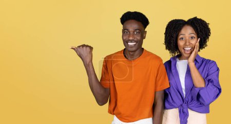 Photo for Positive surprised millennial black couple in casual point hand on empty space, isolated on yellow studio background. Human emotion, surprise, recommendation sale, good news, ad and offer - Royalty Free Image