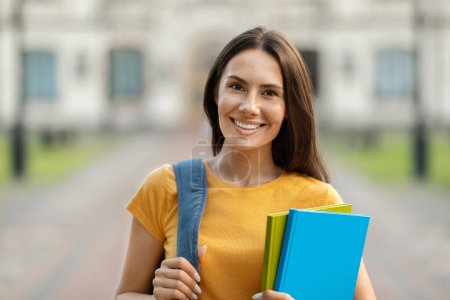 Photo for Cheerful Young Student Woman Holding Workbooks And Posing With Backpack Near College Building Outdoors, Beautiful Millennial Lady Smiling To Camera, Enjoying Studentship And Educational Programs - Royalty Free Image