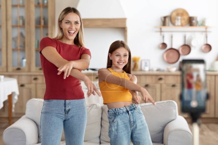 Photo for Excited active mom and preteen daughter kid dancing to music at smartphone frontal camera, recording video, laughing, singing, having fun. Beautiful caucasian mother and child exercising at home - Royalty Free Image
