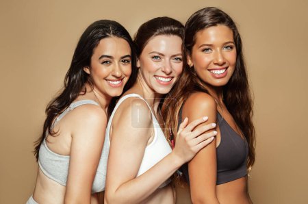 Photo for Happy young arabic, latin and european women in different underwear enjoy free time, natural beauty, isolated on beige background, studio. Lifestyle, health care, freshness - Royalty Free Image