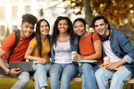 Photo for Student Community. Portrait Of Happy Multiethnic College Friends Posing Together Outdoors, Cheerful Young Men And Women Sitting On Bench In Autumn Park, Looking At Camera And Smiling, Closeup - Royalty Free Image