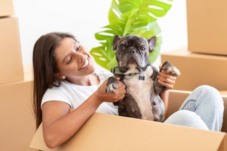 Photo for Closeup of pretty young woman with french bulldog in empty house among cardboxes with belongings, playing with her pet dog in new apartment, enjoying new house. Rent, relocation, moving - Royalty Free Image