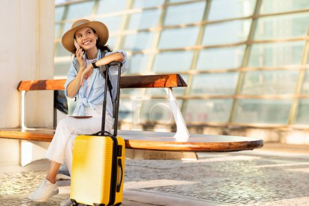 Photo for Cheerful young european woman in hat with suitcase, call by smartphone, enjoy trip at airport, station, wait transport, full length. Good news for tourist, lifestyle in summer, gossip - Royalty Free Image