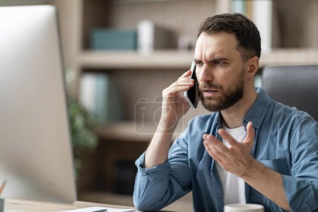 Photo for Worried Young Male Entrepreneur Having Problems With Computer At Work, Talking With Customer Support On Cellphone, Stressed Millennial Businessman Suffering Bad Internet Connection At Workplace - Royalty Free Image