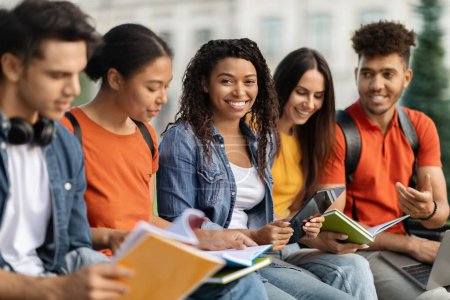 Photo for Beautiful Black Female Student Study Together Outdoors With Her Friends, Group Of Young Happy Men And Women Preparing For Exams, Sitting Outside At Campus, Reading Workbooks, Chatting And Laughing - Royalty Free Image