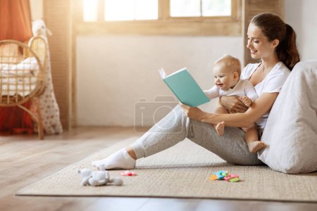 Foto de Feliz madre joven amorosa y su lindo hijo bebé leyendo libro juntos en casa mientras se relaja en el suelo en la habitación de los niños, espacio libre, sol destello. Educación infantil, cuidado infantil, concepto de maternidad - Imagen libre de derechos