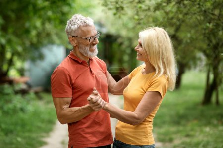 Téléchargez les photos : Romantique aînés conjoints dansant ensemble en plein air dans le jardin d'été, Aimer couple d'âge mûr tenant la main et souriant, S'amuser à l'extérieur, Homme et femme âgés jouissant Lesiure retraite, Copier l'espace - en image libre de droit