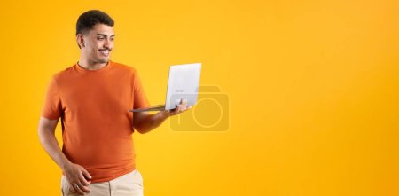 Foto de Hombre brasileño feliz usando ordenador portátil que trabaja en línea o websurf posando sobre fondo amarillo, panorama, espacio de copia. Negocios de tecnología de Internet y carrera independiente - Imagen libre de derechos