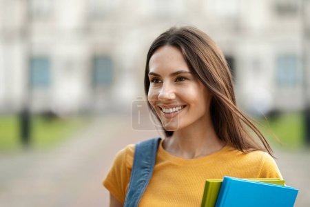 Photo for Closeup Shot Of Beautiful Young Female Student Standing Outdoors, Smiling Millennial Woman With Workbooks And Backpack Relaxing Outside After Classes, Enjoying Studentship, Copy Space - Royalty Free Image