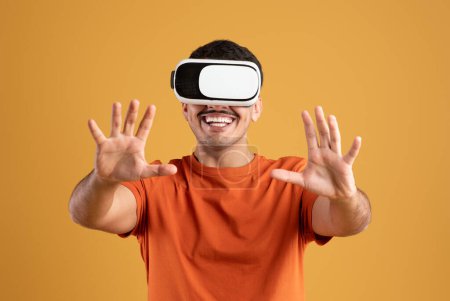 Foto de Jugar aplicaciones de juego móvil en el dispositivo. Hombre brasileño excitado experimentando realidad virtual en gafas vr manos móviles gestos de control, fondo amarillo - Imagen libre de derechos