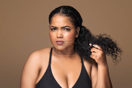 Photo for Split ends. Upset brazilian chubby woman disappointed with her damaged hair, sad lady frowning while looking at camera, standing over brown background - Royalty Free Image