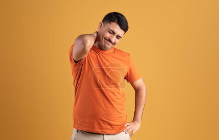 Photo for Sad brazilian man in t-shirt pressing his hand to neck and suffering from muscle pain, posing isolated on yellow studio background. Injured, health problems - Royalty Free Image