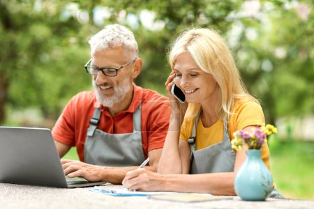 Photo for Remote Business. Happy Mature Couple Using Laptop And Talking On Cellphone Outdoors, Smiling Active Senior Spouses Working Online, Selling Eco-Farming Products, Sitting At Table At Garden Terrace - Royalty Free Image