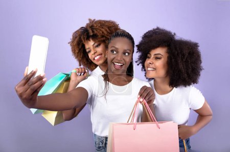 Photo for Three African American Girlfriends Making Selfie Having Fun During Shopping, Posing For Photo Together With Shopper Bags Standing Over Purple Background, Studio Shot. Great Sale Advertisement - Royalty Free Image