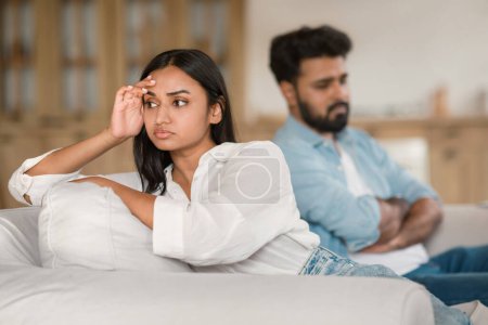 Téléchargez les photos : Jeune couple indien malheureux ayant querelle à la maison, homme et femme déprimés assis sur le canapé, éprouvant des difficultés dans le mariage, accent sélectif sur dame - en image libre de droit