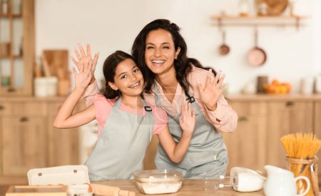 Téléchargez les photos : Joyeux arabe maman et fille cuisson montrant leurs mains en farine dans la cuisine moderne à la maison, pétrissant la pâte pour les cookies ensemble et s'amusant le week-end, souriant à la caméra. Recette de pâtisserie savoureuse - en image libre de droit