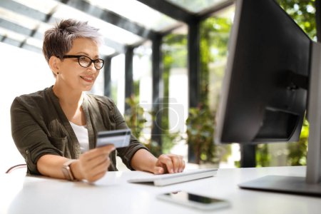 Photo for Cheerful mature woman holding credit card and typing on computer keyboard. Businesswoman or entrepreneur working from home. Online shopping, e-commerce, internet banking, spending money, copy space - Royalty Free Image