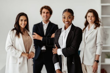 Téléchargez les photos : Équipe d'affaires multiraciale réussie avec une dirigeante noire debout au bureau et souriant à la caméra. Travail d'équipe et concept de réussite professionnelle - en image libre de droit