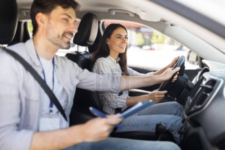 Photo for Driving school. Handsome man instructor examinating happy lady student, taking notes at chart while sitting by cheerful brunette woman driving auto, holding steering wheel, side view, copy space - Royalty Free Image